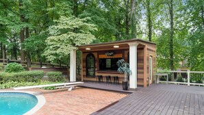 Ein hölzerner Pavillon mit Pool und Terrassenbereich, umgeben von Bäumen.