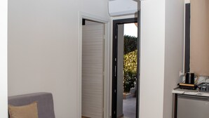 Una sala de estar moderna con un sofá gris, una mesita de centro y una cocina con un refrigerador y una cafetera.