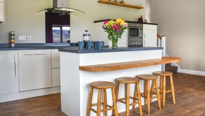 A modern kitchen with a central island, wooden stools, a coffee maker, and a flower vase. - 2 bedroom accommodation in Rathmell, near Settle (Rathmell, near Settle)
