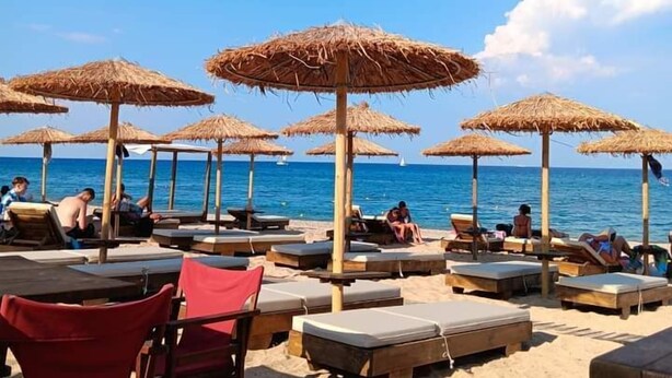 Ein Strandloungebereich mit Reetdachschirmen und Liegestühlen mit Blick auf das Meer.