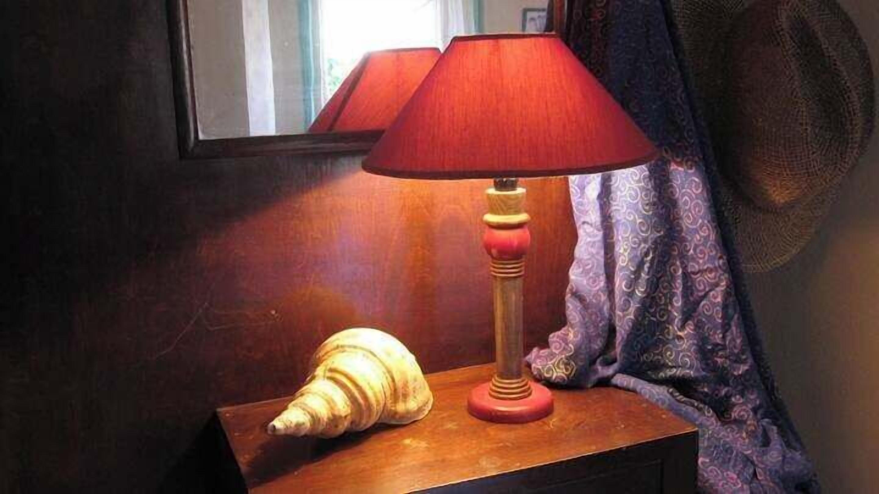 A wooden nightstand with a red lamp and a seashell.