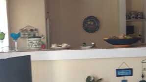 Ein Wohnzimmer mit Holzboden, einem Fernseher auf einem Beistelltisch, einem Ventilator und einem Regal mit Dekoration.