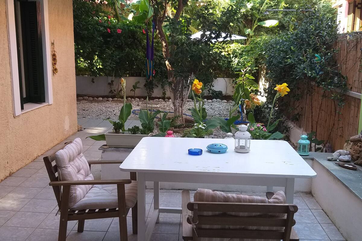 A patio with a white table, two striped chairs, and a small garden area with flowers and a wooden fence.