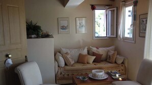 Ein gemütliches Wohnzimmer mit einer Couch, zwei Sesseln, einem Couchtisch und einem Fenster mit Vorhängen.