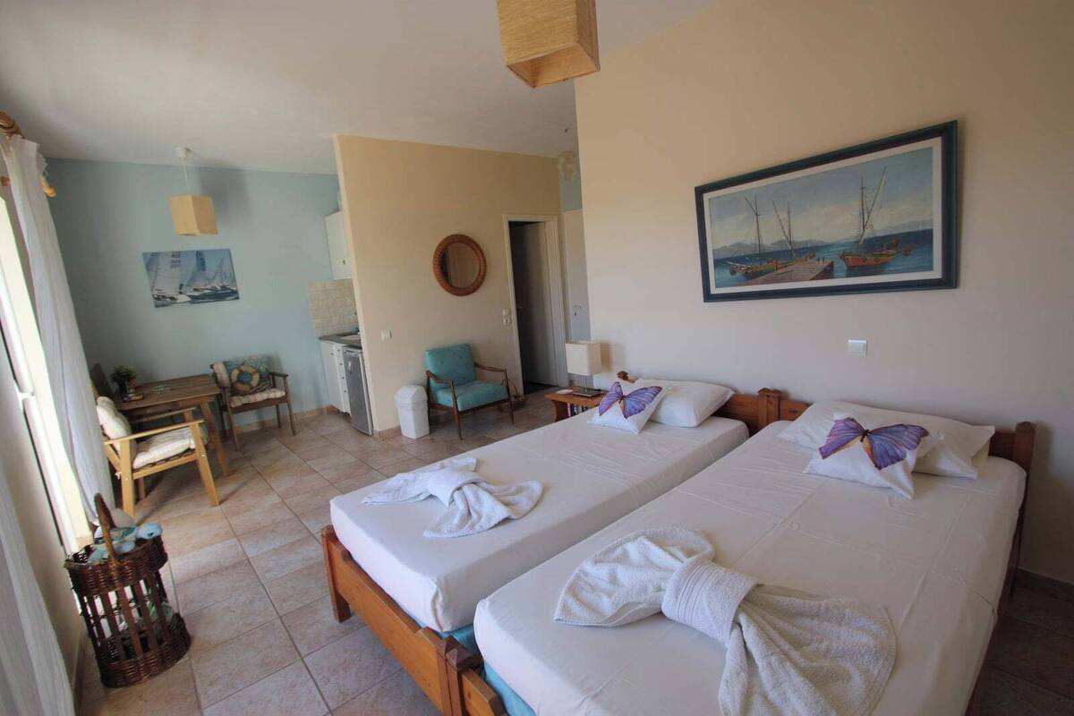 A hotel room with two beds, a desk, a chair, a small kitchenette, and a painting on the wall.