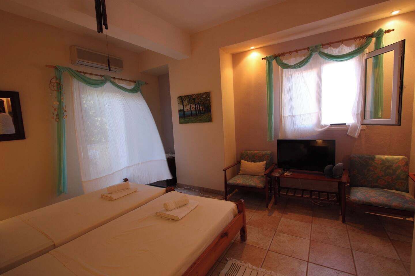 A hotel room with a bed, two chairs, a TV, and a window with curtains.