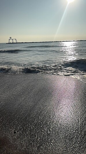 A beach with a structure in the distance and the sun shining over the water.
