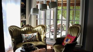 A room with two upholstered armchairs, a glass coffee table, and a large window with a view of greenery.