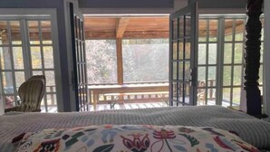 A bedroom with a bed, a chair, and a view of a deck through open doors.