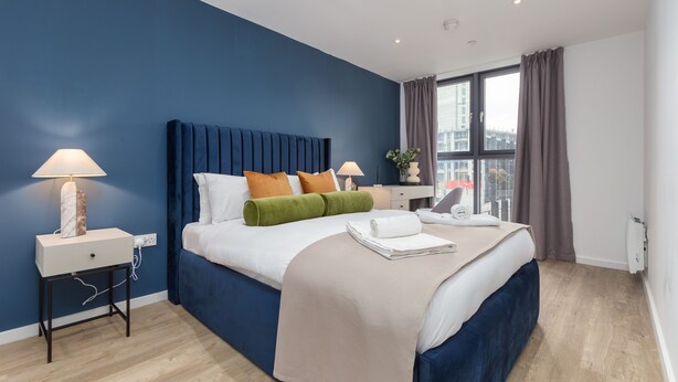 Een moderne hotelkamer met een groot bed, een nachtkastje, een bureau en een raam met gordijnen.