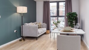Een moderne woonkamer met een grijze bank, een vloerlamp en een eettafel met borden en glazen.