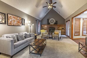 A spacious living room with a gray sofa, a wooden coffee table, striped armchairs, a fireplace, and a ceiling fan. - Suburban Farmhouse w/ Match Soccer Vibes (Overland Park)