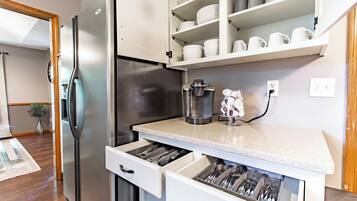 Una cucina con frigorifero in acciaio inox, mobili bianchi e un piano di lavoro con macchina da caffè e utensili.