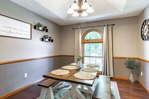 A dining area with a long wooden table, woven placemats, a chandelier, a clock, and a window with curtains. - Suburban Farmhouse w/ Match Soccer Vibes (Overland Park)