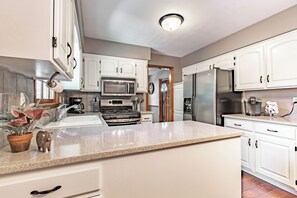 A modern kitchen with white cabinets, stainless steel appliances, a granite countertop, and a visible clock. - Suburban Farmhouse w/ Match Soccer Vibes (Overland Park)