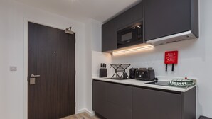 A compact kitchen with dark cabinets, a microwave, and a fire safety sign. - Spacious City Studio (Manchester)