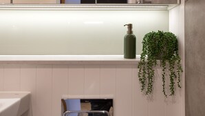 A bathroom with a white tiled wall, a green bottle on a shelf, and a hanging plant. - Spacious City Studio (Manchester)