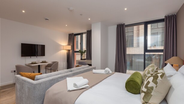 A modern hotel room with a large bed, a sofa, a desk, and a TV. - Spacious City Studio (Manchester)