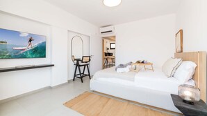 A modern bedroom with a large bed, a flat-screen TV on the wall, a small table with a lamp, and a view of the ocean through the window. - Finikoudes Marina View 202 - Charming Larnaca Centre Getaway (Larnaca)