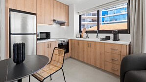 A modern kitchen with wooden cabinets, a black dining table, and a view of a building through the window. - Finikoudes Marina View 201 - Charming Finikoudes Getaway (Larnaca)