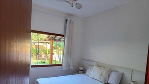 A bedroom with a bed, a window, a ceiling fan, and a nightstand. - Charming Refuge: Arraial House (Arraial d'Ajuda)