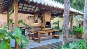 A rustic outdoor kitchen with a wooden table and benches, surrounded by tropical plants. - Charming Refuge: Arraial House (Arraial d'Ajuda)