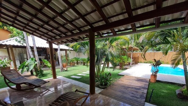 An outdoor patio with wooden furniture, a pool, and tropical plants. - Charming Refuge: Arraial House (Arraial d'Ajuda)