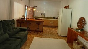 A compact living space with a sofa, a dining area with chairs, a kitchen with a refrigerator, and a decorative item on the wall. - Charming Refuge: Arraial House (Arraial d'Ajuda)