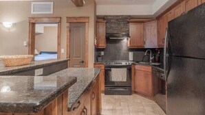 Une cuisine avec des meubles en bois, des plans de travail en granit, un réfrigérateur noir et un four encastré.