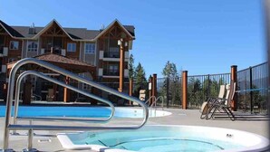 Une piscine avec un escalier en métal, des chaises longues et une zone délimitée par une clôture.