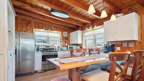 A wooden interior with a dining table, chairs, and a kitchen area. - Look and Sea: Dog-friendly Ocean View Cottage with Pool Table (Oak Island)