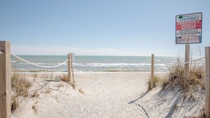A beach entrance with a sign indicating emergency vehicle access and a rope barrier. - Look and Sea: Dog-friendly Ocean View Cottage with Pool Table (Oak Island)