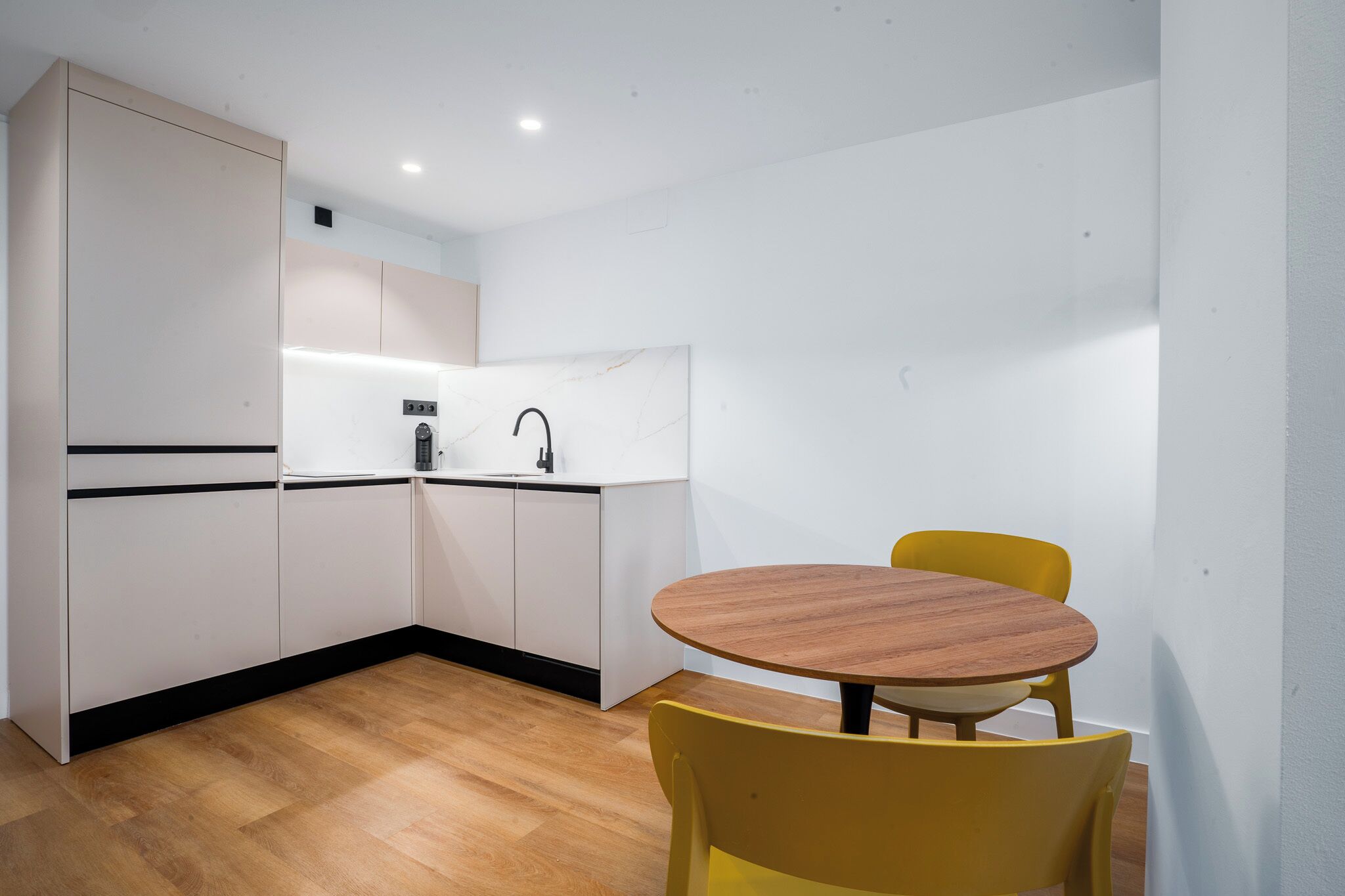 Una cucina compatta con mobili bianchi, un tavolo da pranzo in legno e sedie gialle.
