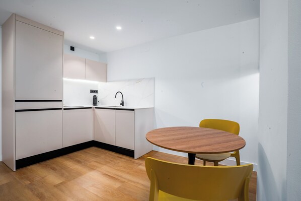Une cuisine de taille réduite avec des meubles blancs, une table à manger en bois et des chaises jaunes.