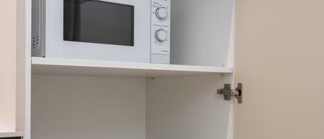 A kitchen with a microwave on the upper shelf, white bowls and plates on the middle shelf, and a stainless steel pot on the lower shelf.
