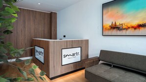 Ein Empfangstresen mit 'smarttr'-Branding, eine Wandpaneele aus Holz, ein grünes Sofa und ein Stadtbildgemälde.