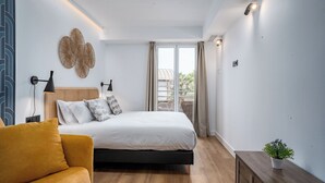 Ein Schlafzimmer mit Bett, Nachttisch, Lampe, einer Pflanze und Blick ins Freie.