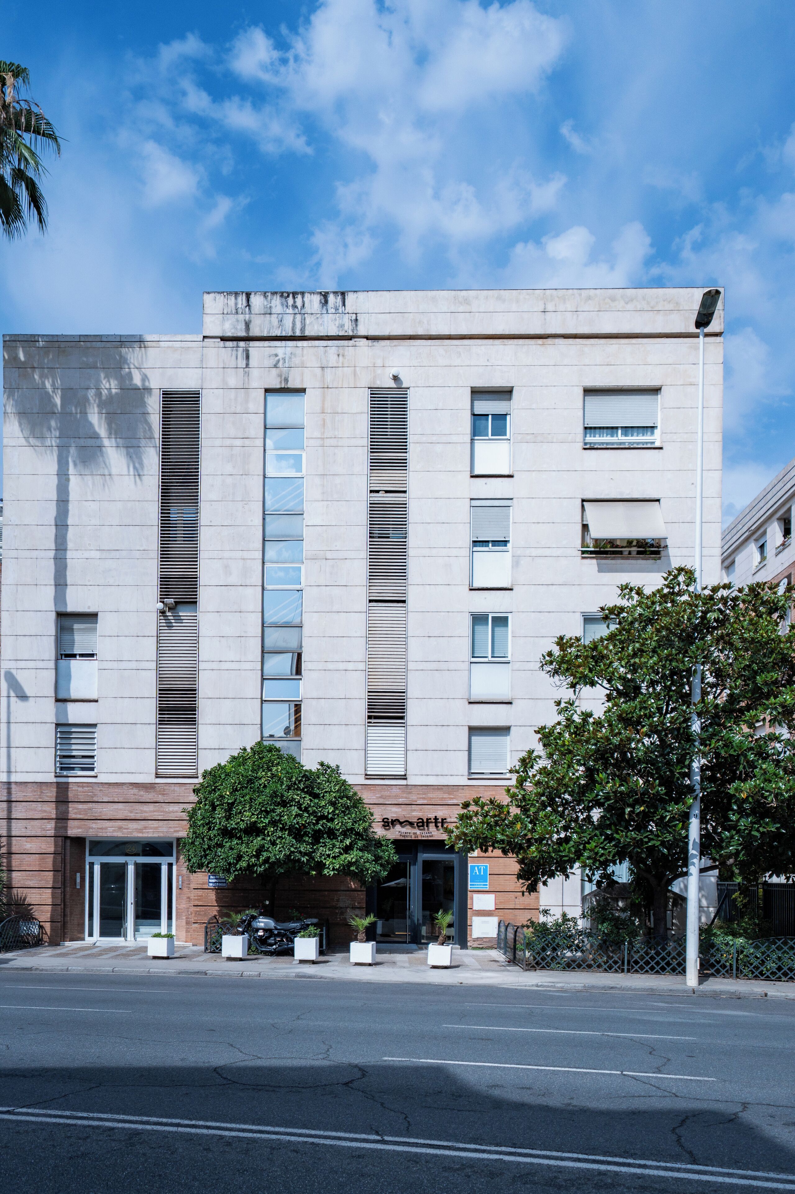 A modern building with a flat facade, large windows, and a central entrance with a tree.