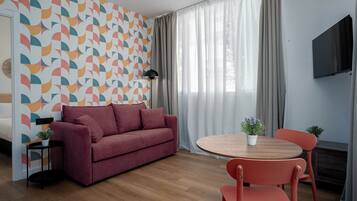 Een moderne kamer met een behang, een bank, een tafel met stoelen, een televisie en een raam met gordijnen.