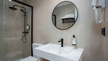 Une salle de bain moderne avec une douche à parois de verre, un lavabo blanc doté d’un robinet noir et un miroir rond placé au-dessus.