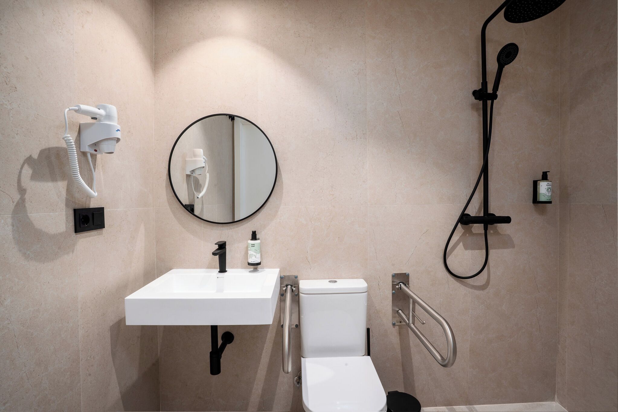 A modern bathroom with a white sink, round mirror, toilet, and handheld showerhead.