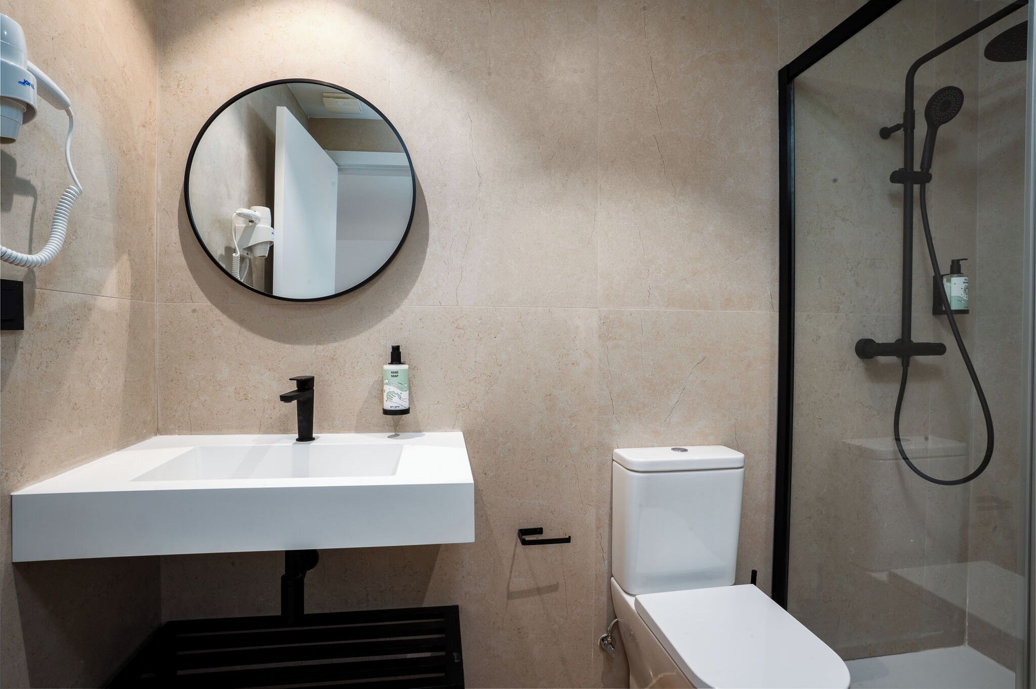 Une salle de bain avec un lavabo blanc, un miroir rond, des toilettes et une douche à parois de verre.