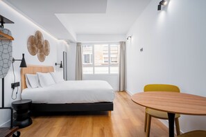 A modern bedroom with a bed, bedside table, lamp, and a round wooden table with a chair. - Smartr Puente de Triana (Seville)