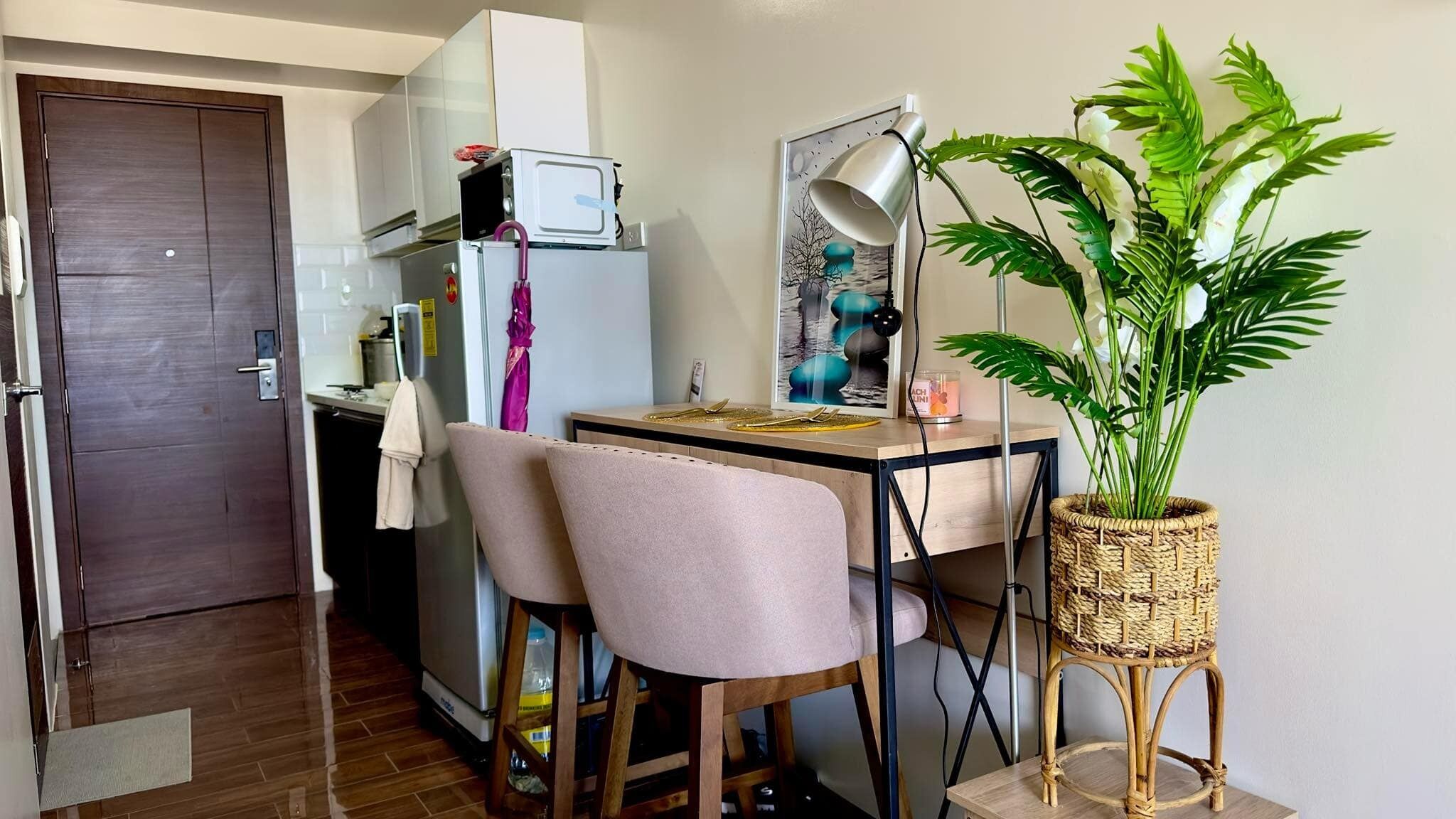 Una cocina compacta con microondas, refrigerador y un pequeño comedor con dos sillas y una mesa.