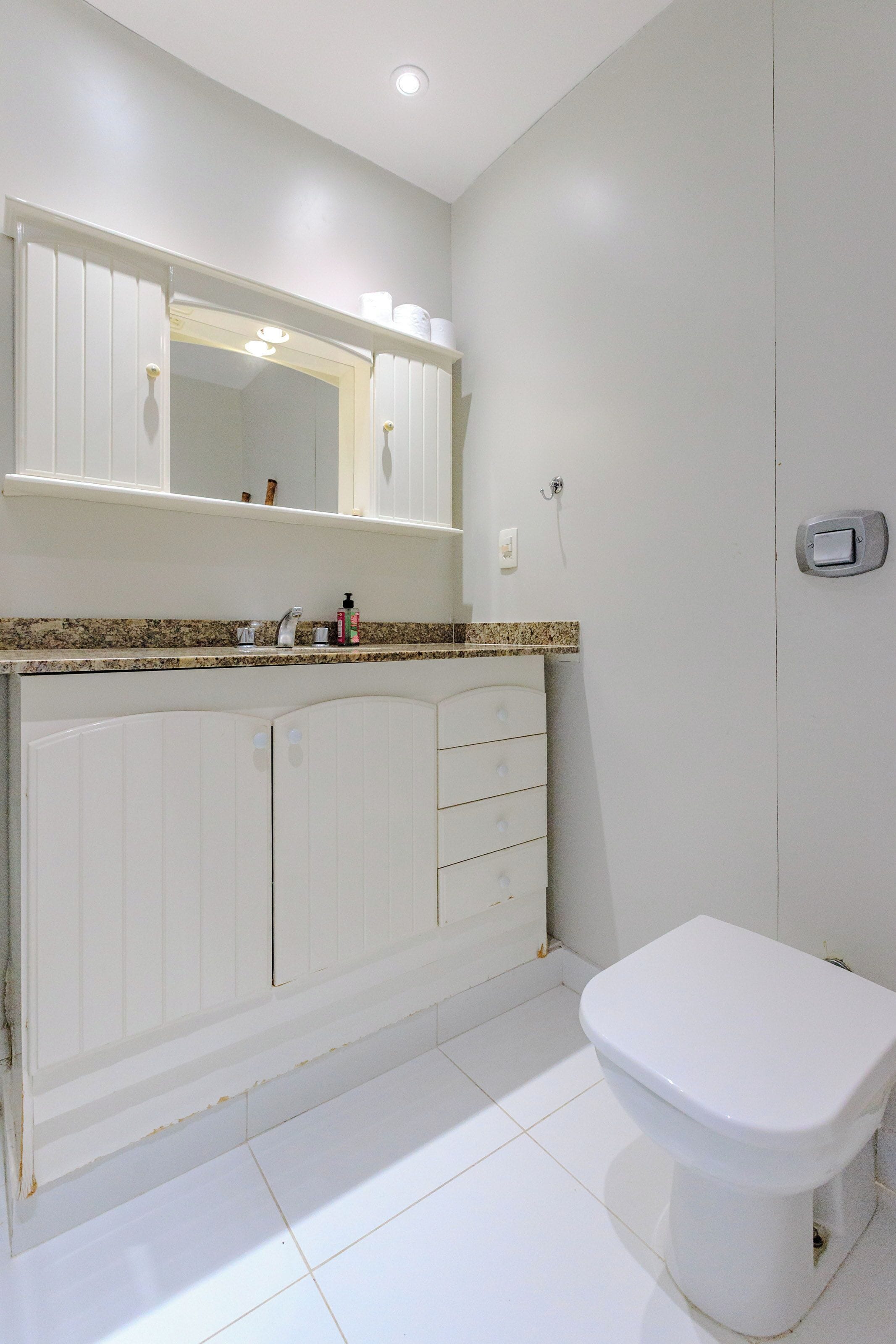 A bathroom with a white toilet, a vanity with a mirror, and a sink.
