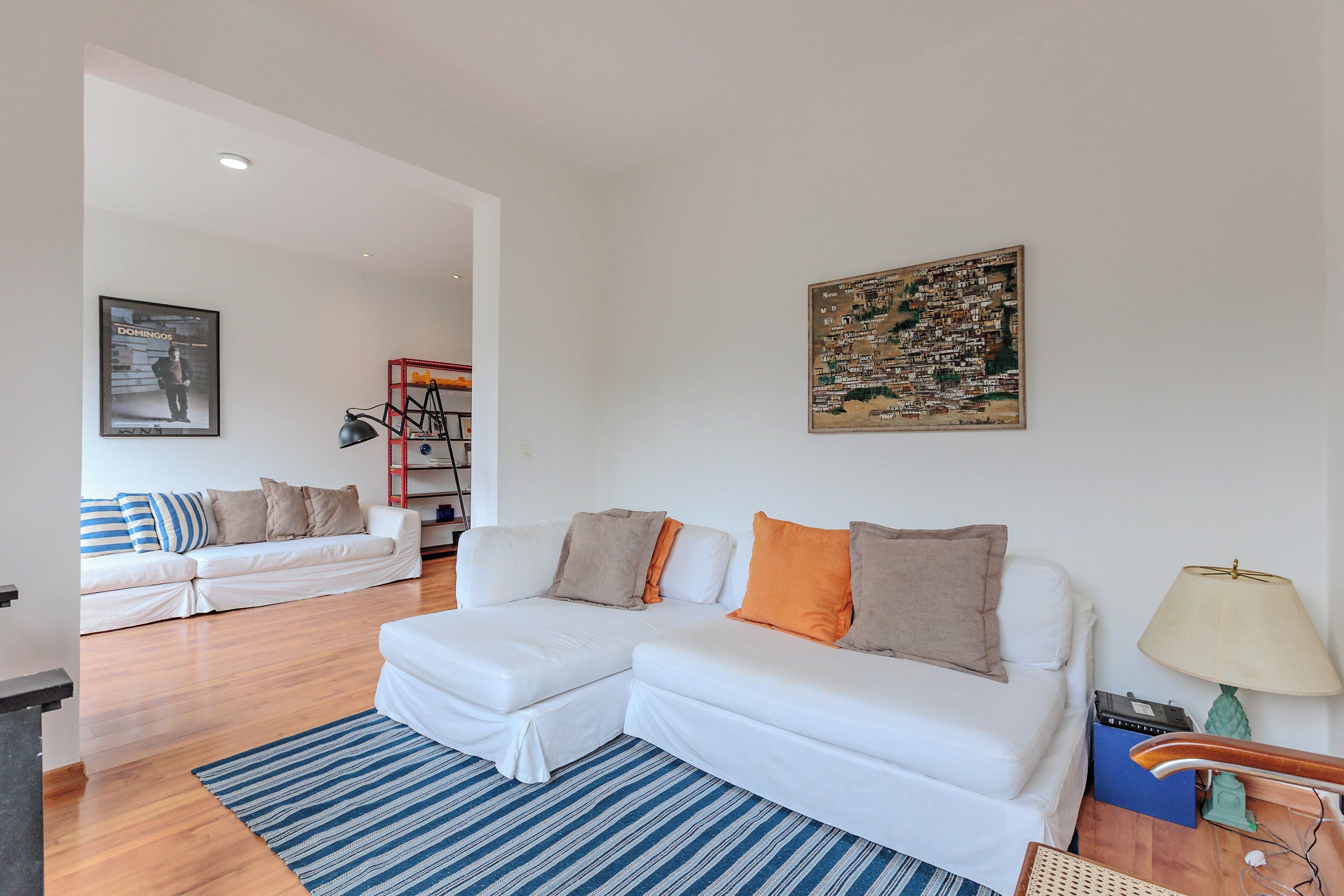 A modern living room with a white sofa, a blue striped rug, and a cityscape painting on the wall.