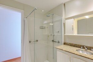 Een moderne badkamer met een glazen douchecabine, een wastafel met granieten blad en een grote spiegel erboven.
