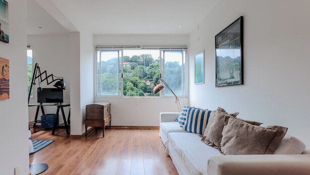 A modern living room with a large window, a white sofa, and a desk with a lamp. - Vista Carioca (Rio de Janeiro)