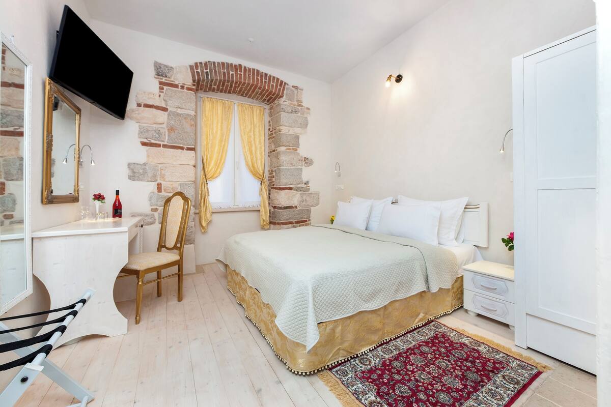 A bedroom with a bed, bedside table, chair, and a TV mounted on the wall.