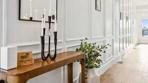 A hallway with white walls, a wooden console table with a WiFi sign, black candle holders, and a potted plant. - Luxury Spa Retreat | Sauna, Hot Tub & Fire Pit (Nashville)